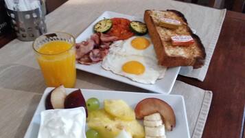 A breakfast plate with eggs, bacon, toast, and fruit, and a glass of orange juice on a table.