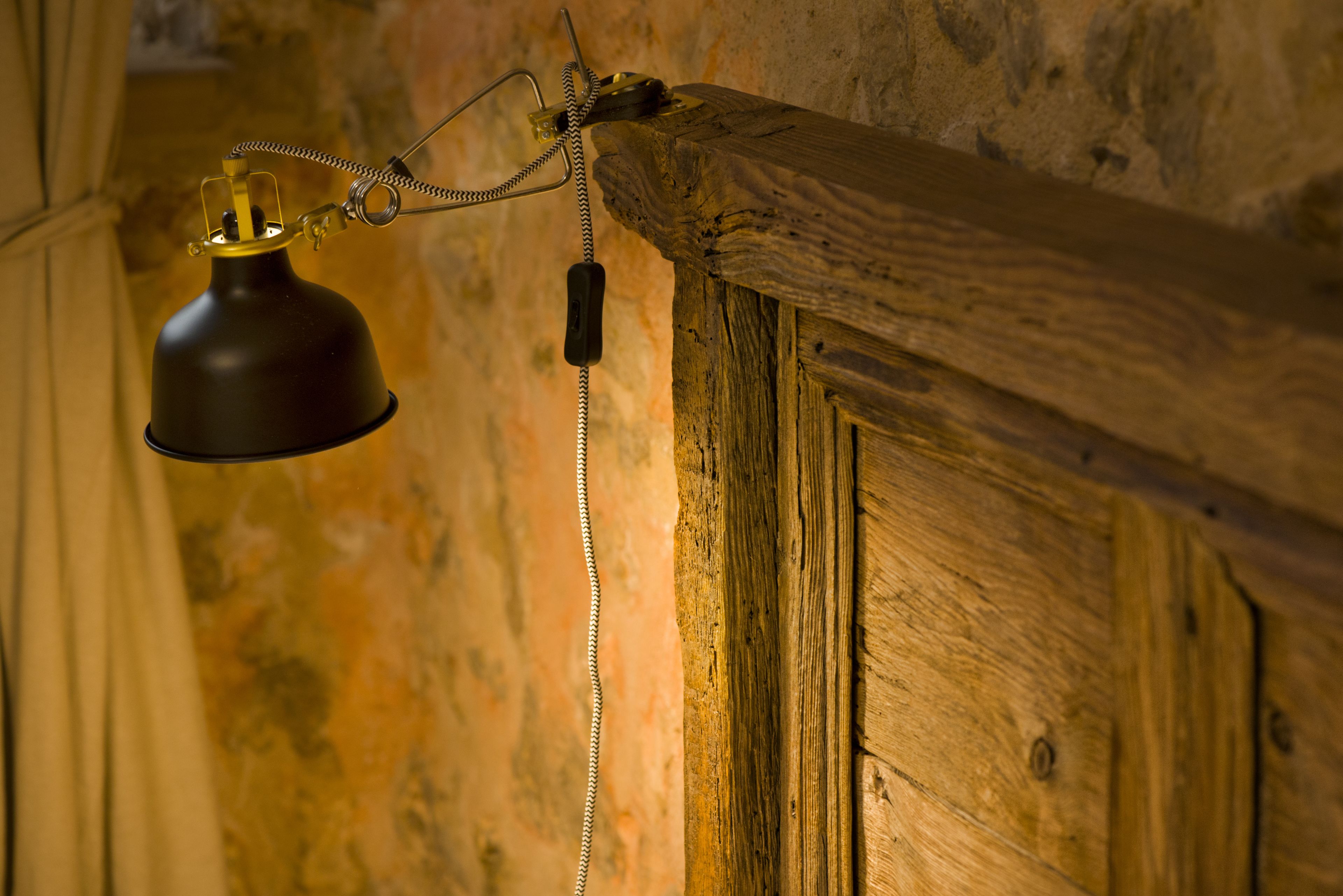 A vintage-style desk lamp with a coiled cord hanging from a wooden beam.