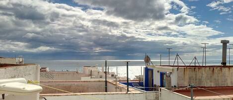 A rooftop with a view of the sea, featuring buildings with satellite dishes and a blue door.