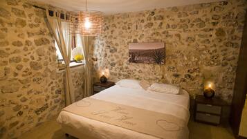 A bedroom with a stone wall, a bed with a heart-shaped bedspread, and a nightstand with a lamp.