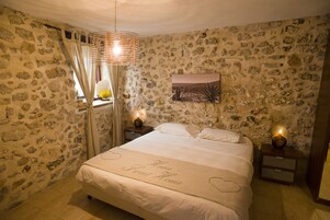 Un dormitorio con pared de piedra, una cama con cubrecama con forma de corazón y una mesita de noche con lámpara.