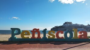 Letrero de playa que dice 'Peníscola', con un pueblo costero y un castillo al fondo.