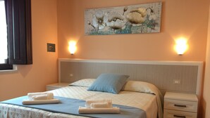 A neatly made bed with a patterned bedspread, two pillows, and two folded towels. There is a nightstand with a drawer and a wall-mounted light. - Agriturismo I Tre Ulivi (Paternopoli)