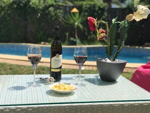 A table with two wine glasses, a bottle of wine, a bowl of fruit, and a potted plant by a pool. - Maison de Luxe Pour Toute la Famille (Hammamet)