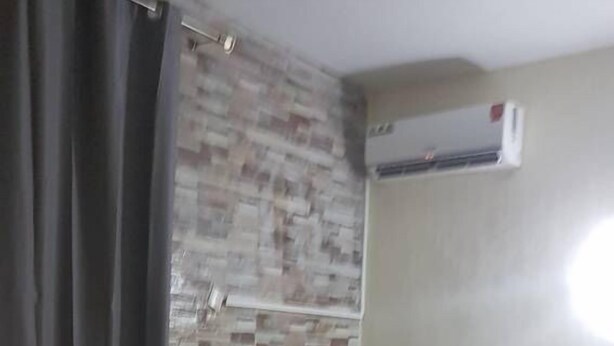 A bedroom with a bed, a curtain, a wall-mounted air conditioner, and a tiled floor.