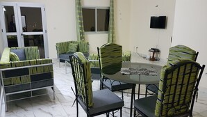 A dining area with a round table and chairs, a television mounted on the wall, and a window with curtains.
