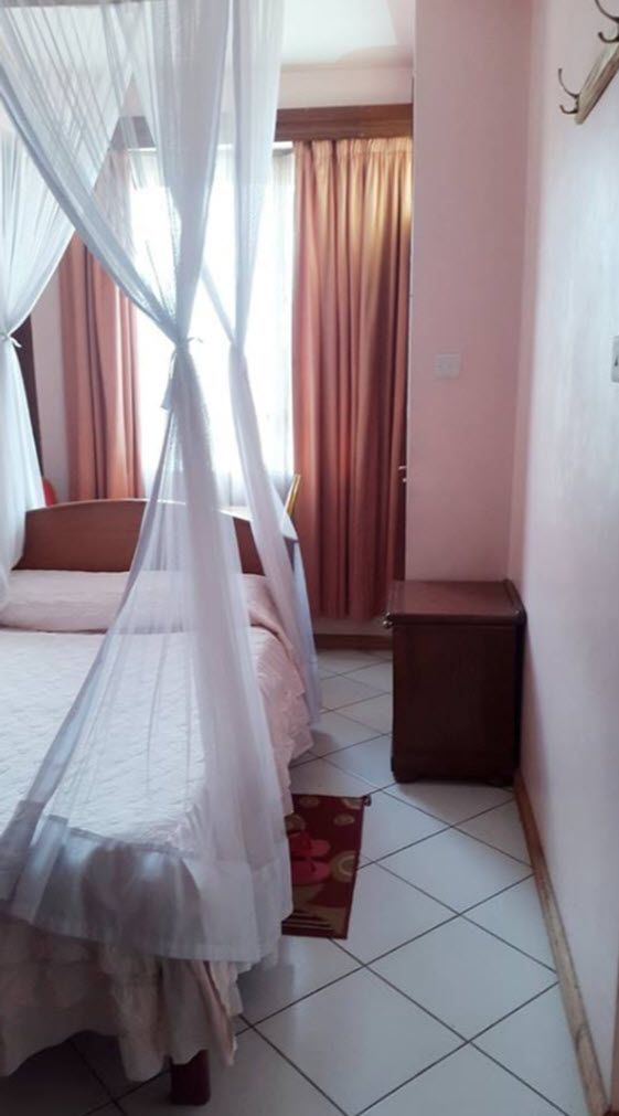 Une chambre à coucher avec un lit sous un baldaquin, une table de chevet, une petite armoire et une fenêtre avec des rideaux.