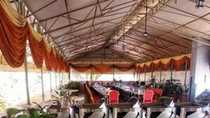 A covered outdoor area with tables set up for dining, a large potted plant, and a tiled floor. - Sagas Hotel Ltd (Nairobi)
