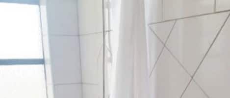 Een kleine, witte badkamer met douchegordijn, toilet en raam.