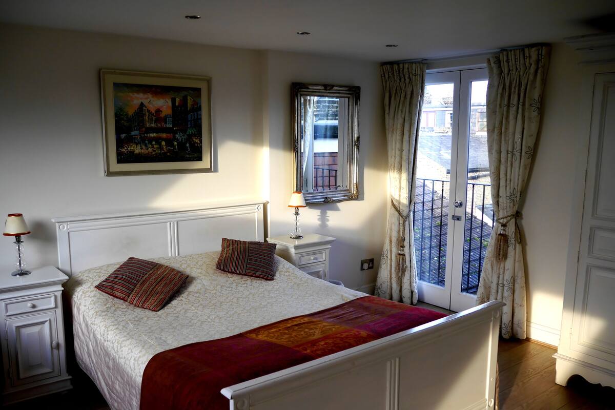 A neatly arranged bedroom with a bed, bedside tables, a mirror, and a window with curtains.