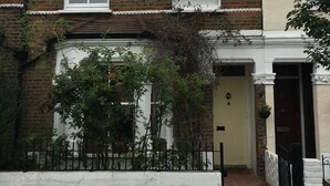 A two-story brick house with a white front door, a small garden, and a black metal fence. - Goodenough Guesthouse (London)