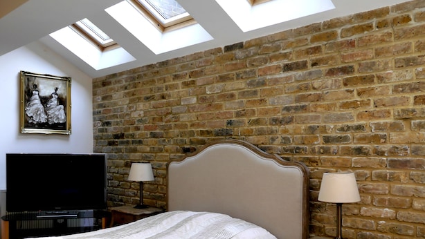 A bedroom with a brick wall, a large bed, a television, and skylights. - Goodenough Guesthouse (London)