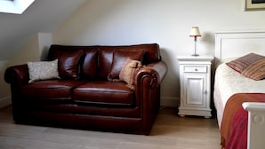 A cozy room with a brown leather sofa, a white bedside table with a lamp, and a bed with a patterned blanket. - Goodenough Guesthouse (London)