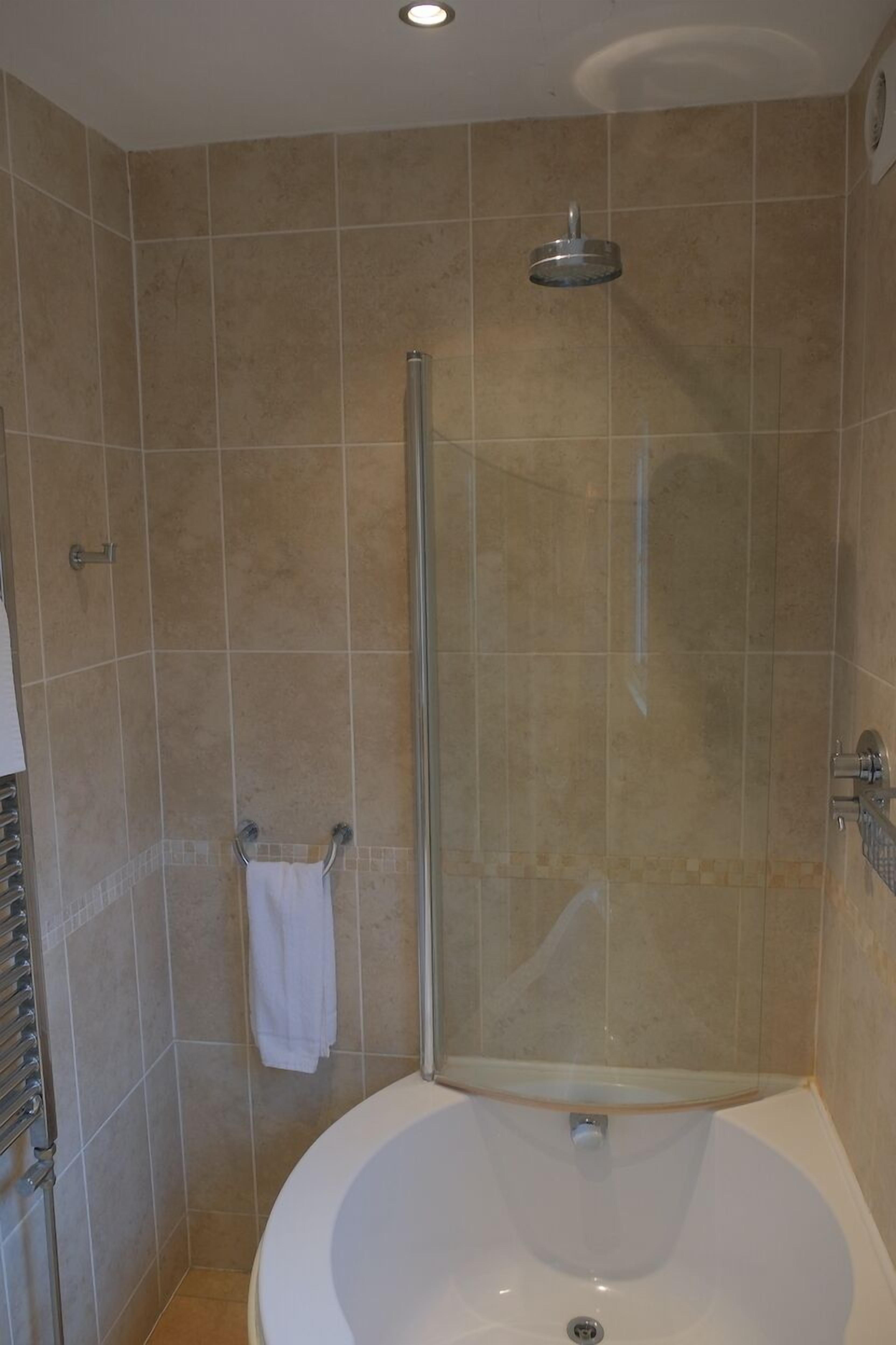 A bathroom with a glass-enclosed shower, a white bathtub, and beige tiled walls.
