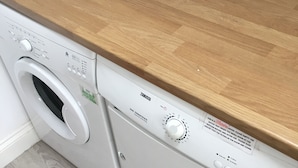 A front-loading washing machine with a wooden countertop above it. - Goodenough Guesthouse (London)