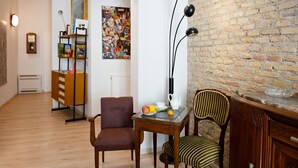 Una habitación con pared de ladrillo, una mesa de madera con tetera, dos sillas, una estantería y un cartel en la pared.