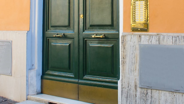 Puerta doble verde con un ventanal decorativo encima, un letrero con el número '55' y una pequeña placa en la pared.