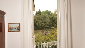 Una habitación con una silla roja, un pequeño armario de madera y vistas a un balcón con barandilla.