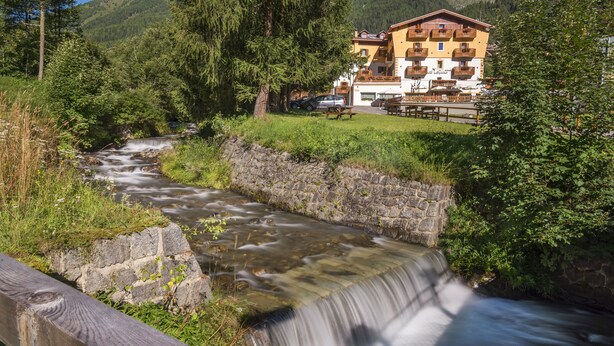 Ein Hotel mit einer Steinmauer, einem kleinen Bach und einer Bergkulisse.