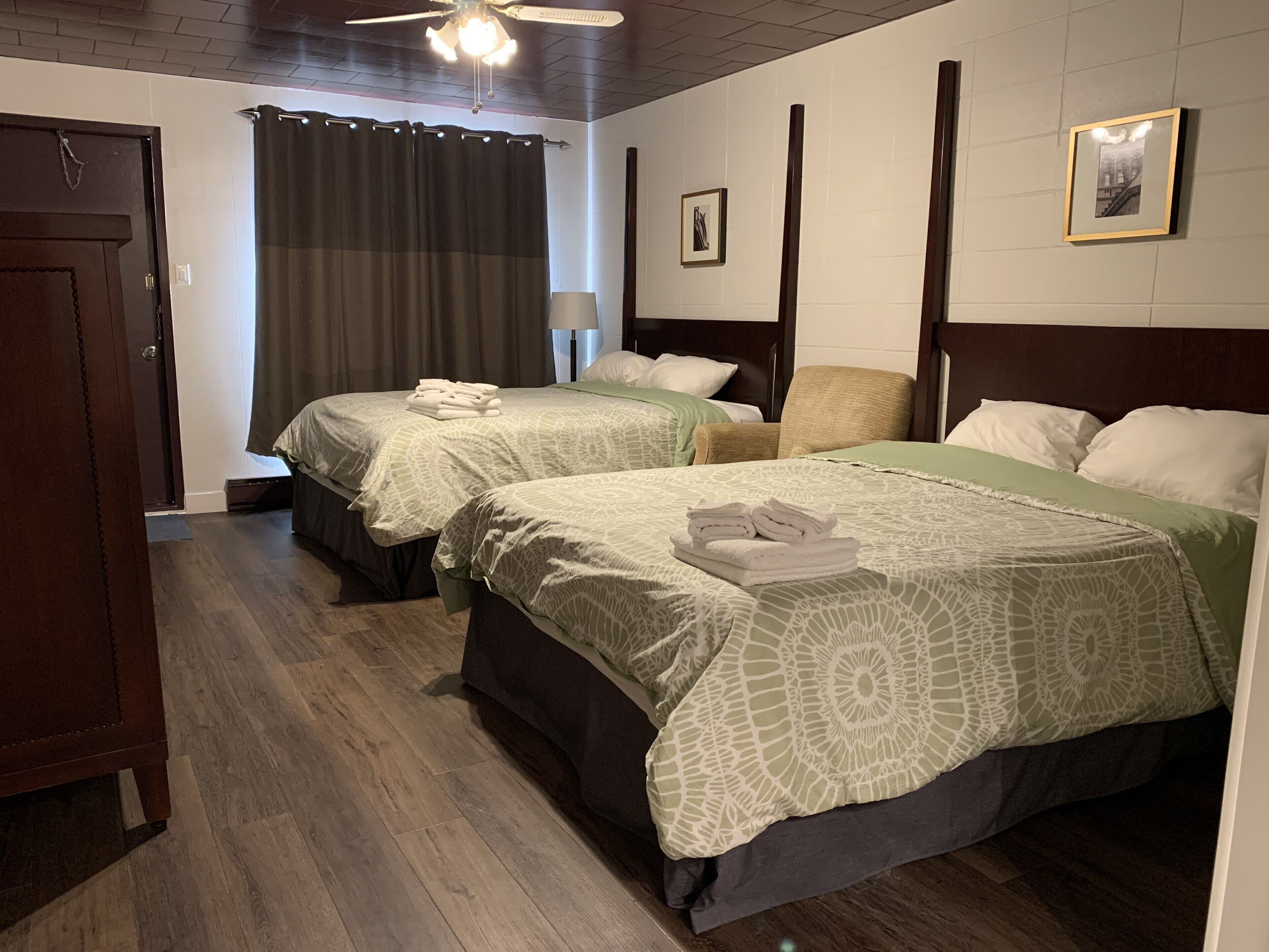 A hotel room with two beds, a ceiling fan, a window with curtains, and a framed picture on the wall.