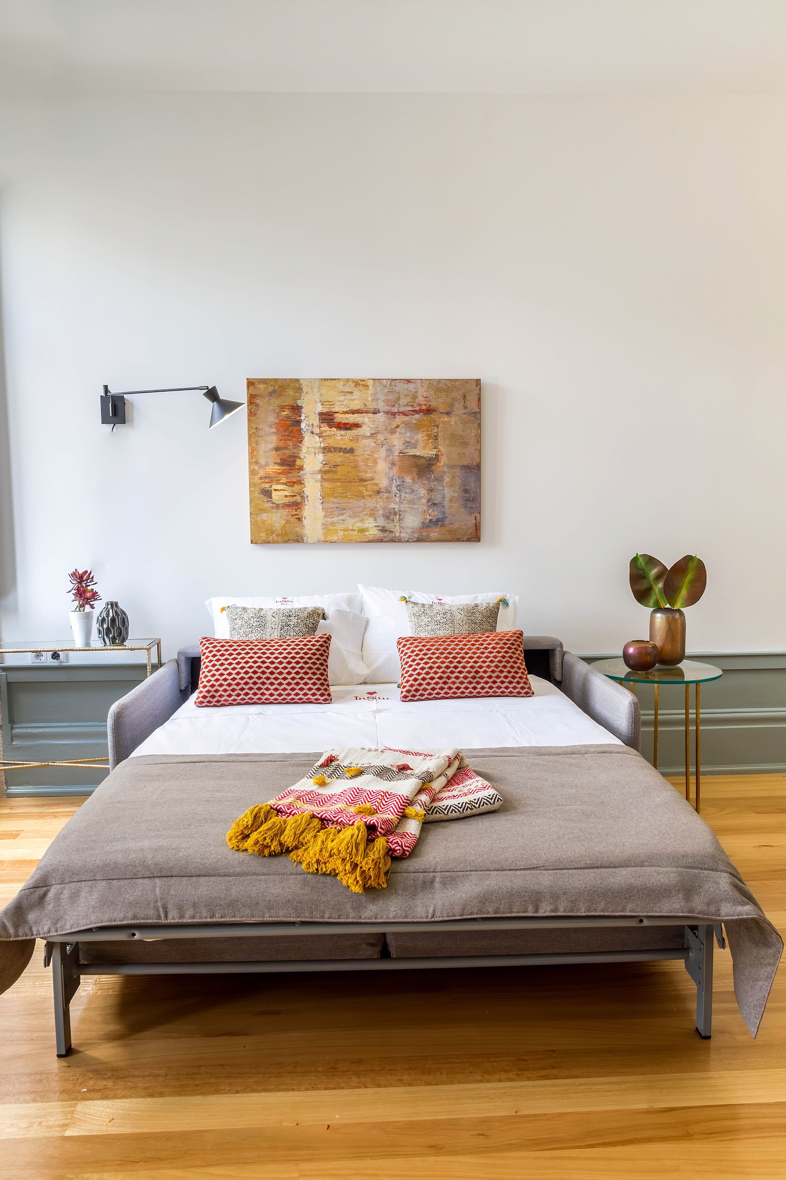 A modern bedroom with a large bed, a bedside table, a small side table, and a wall-mounted lamp.