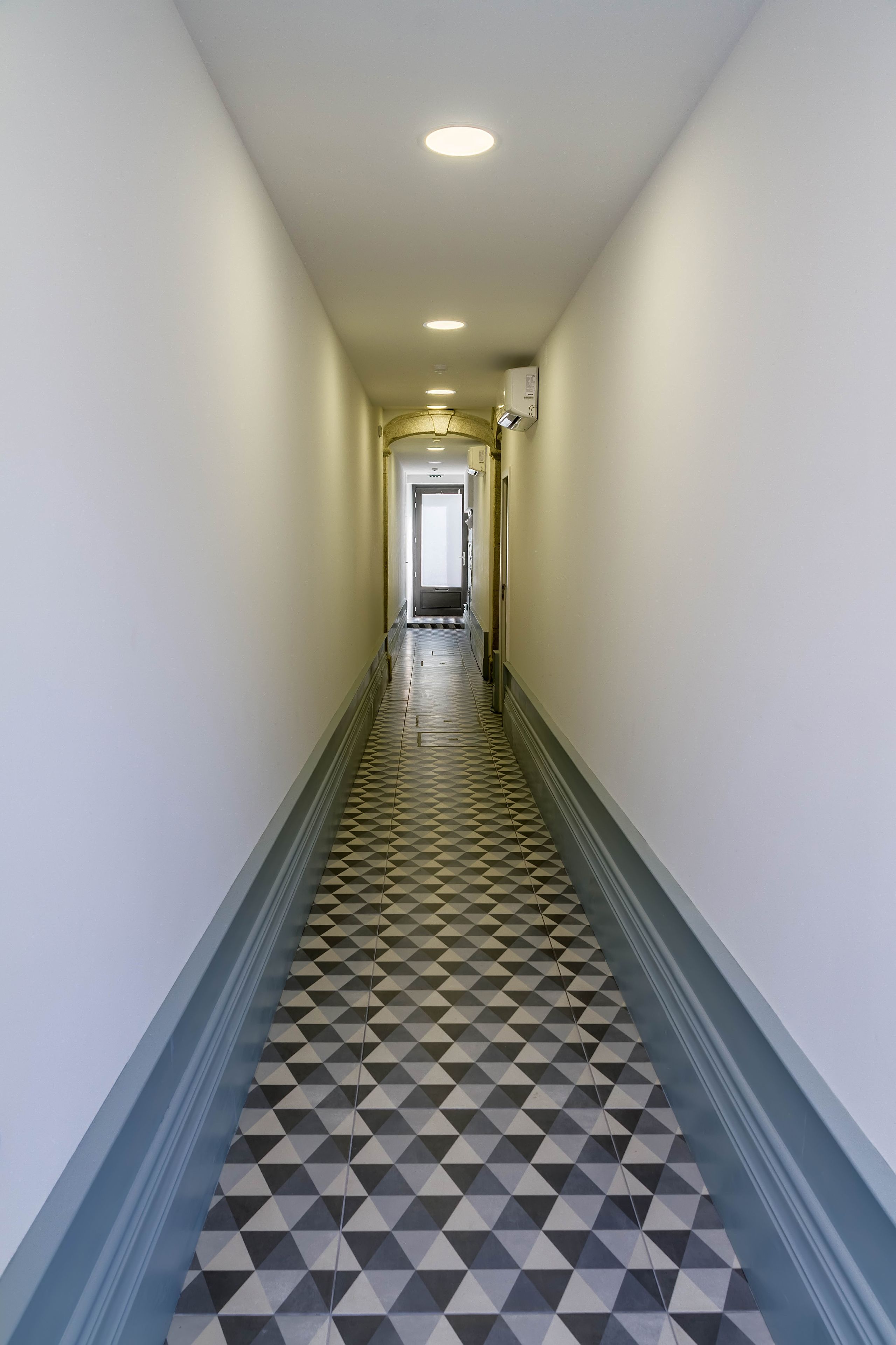 En hall med ett golv i geometriskt mönster, vita väggar och ett tak med infälld belysning.
