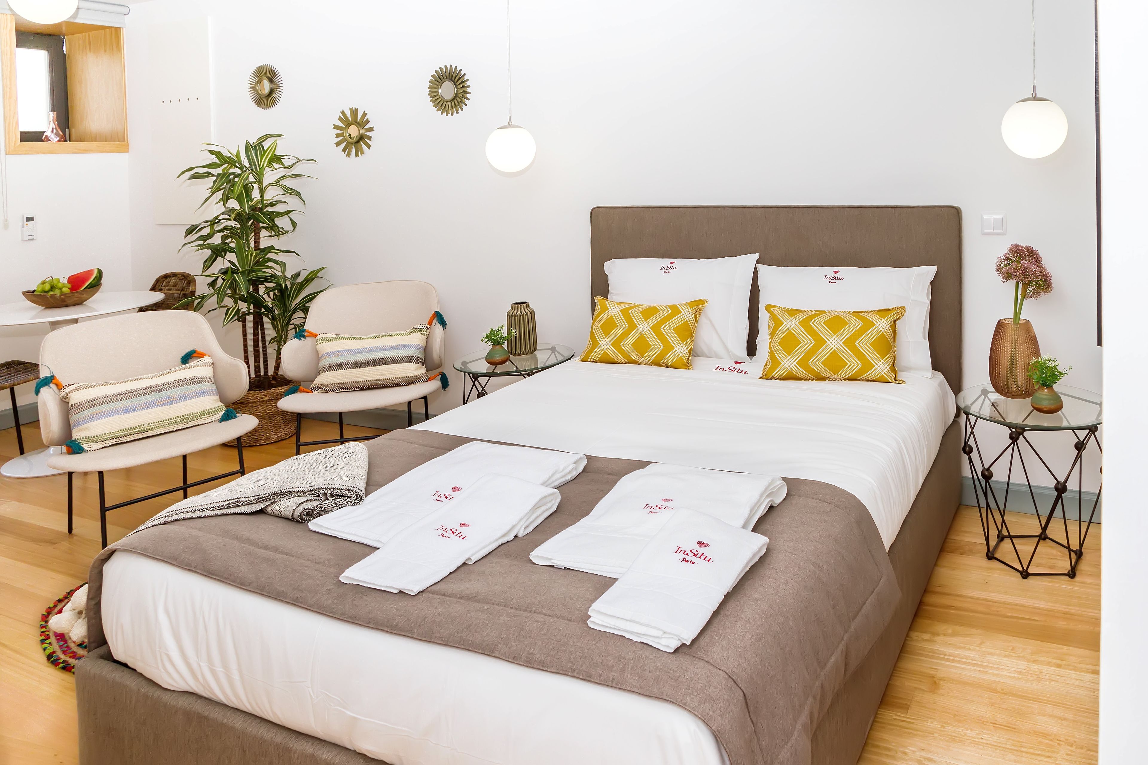 Een netjes ingerichte hotelkamer met een bed, stoelen, een tafeltje en een bloempot.