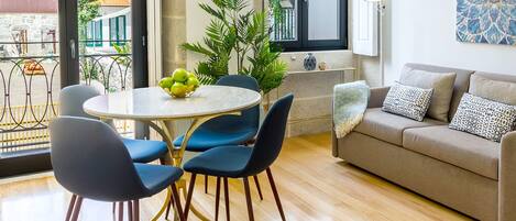 A modern living room with a round table, blue chairs, a grey sofa, and a balcony with a view of buildings.