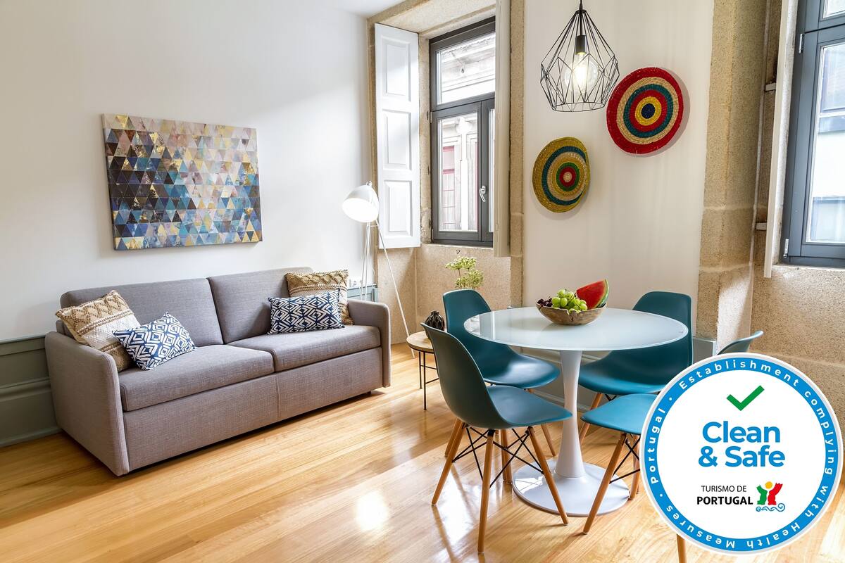 A modern living room with a grey sofa, blue chairs, a round table, and a colorful abstract painting.