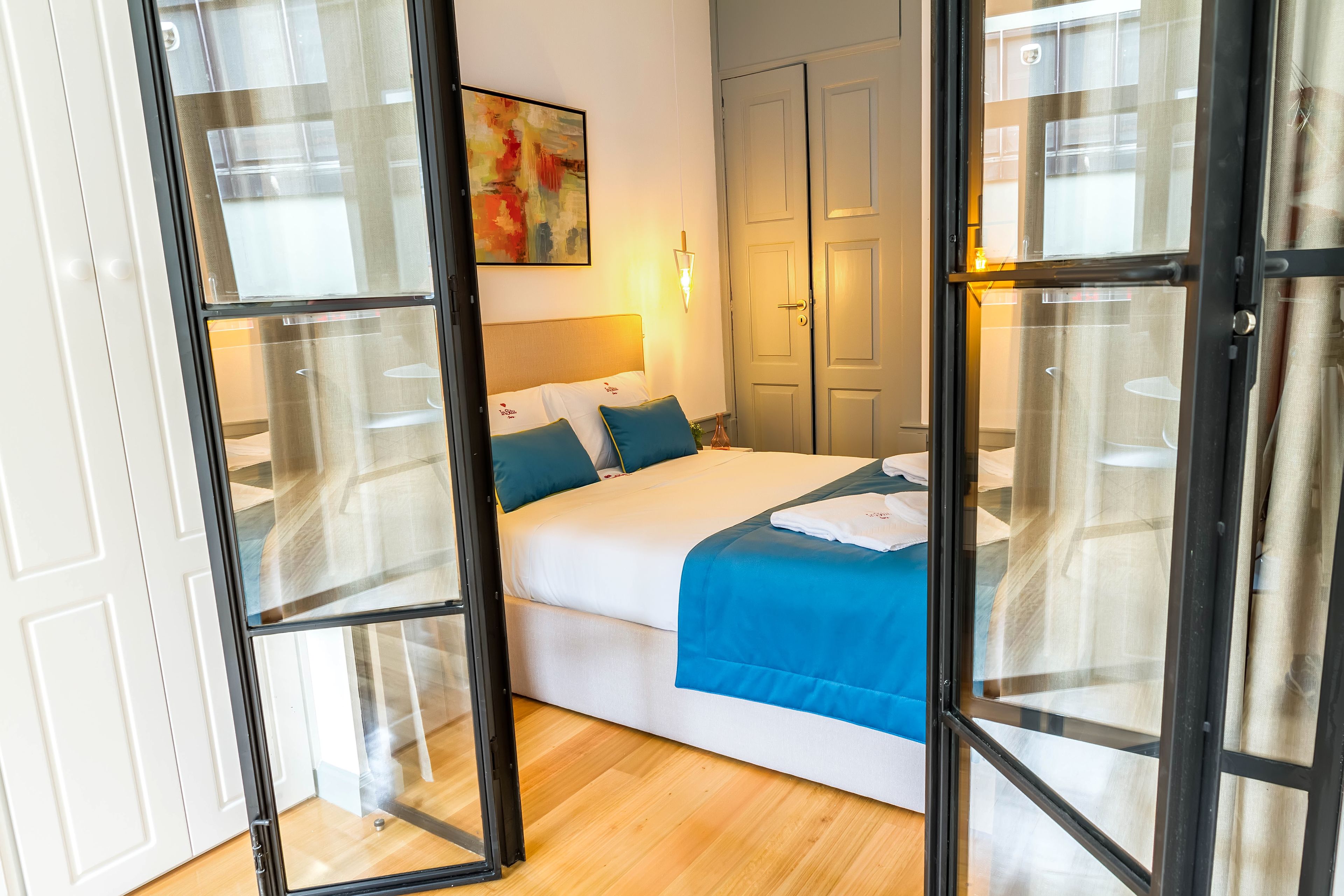 A bedroom with a bed, a nightstand, a wall-mounted lamp, and a door with glass panels.