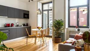 Una cuina moderna amb armaris grisos, una zona de menjador amb taula rodona i cadires de vimetla, un sofà amb vistes a l'exterior i una planta en test.