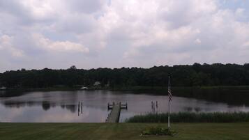A calm lake with a dock extending into the water, surrounded by lush greenery and a forested hill in the background.