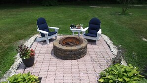 A fire pit surrounded by two white chairs with blue cushions, a small table, and potted plants. - Marvel's on the Creek (East New Market)