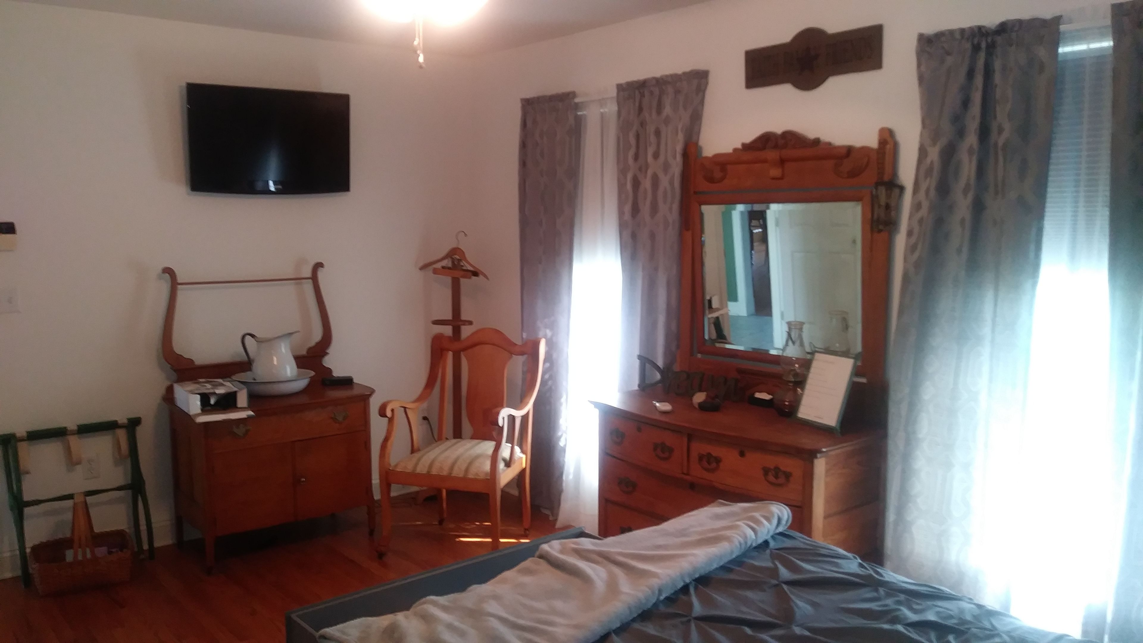 A bedroom with a bed, wooden dresser, chair, and a television on the wall.