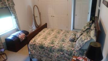 Une chambre à coucher avec une couvre-lit à motifs floraux, une tête de lit en bois, une table de chevet avec une lampe et une commode.