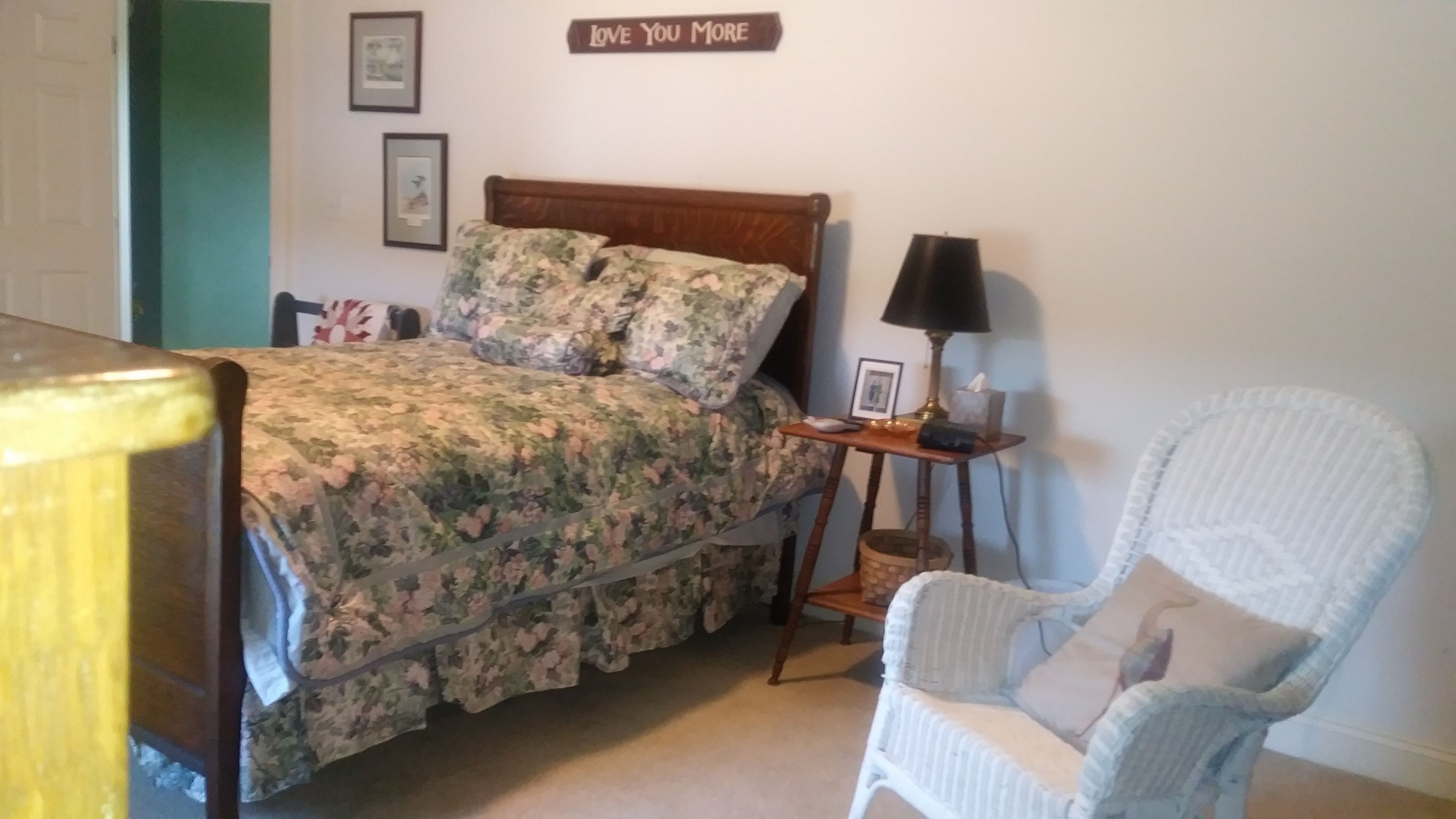 A bedroom with a bed, a bedside table with a lamp, a chair, and a wall sign.
