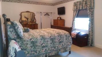A bedroom with a floral bedspread, a wooden dresser, a mirror, and a television on the wall.