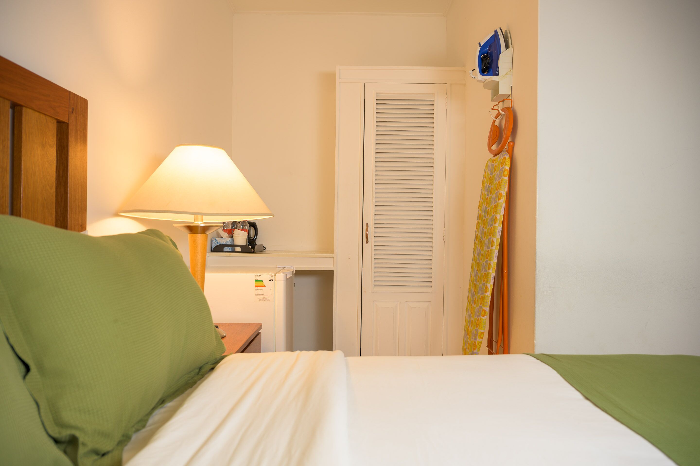 A hotel room with a bed, a nightstand with a lamp, a wardrobe, and a door with a towel hanging on it.