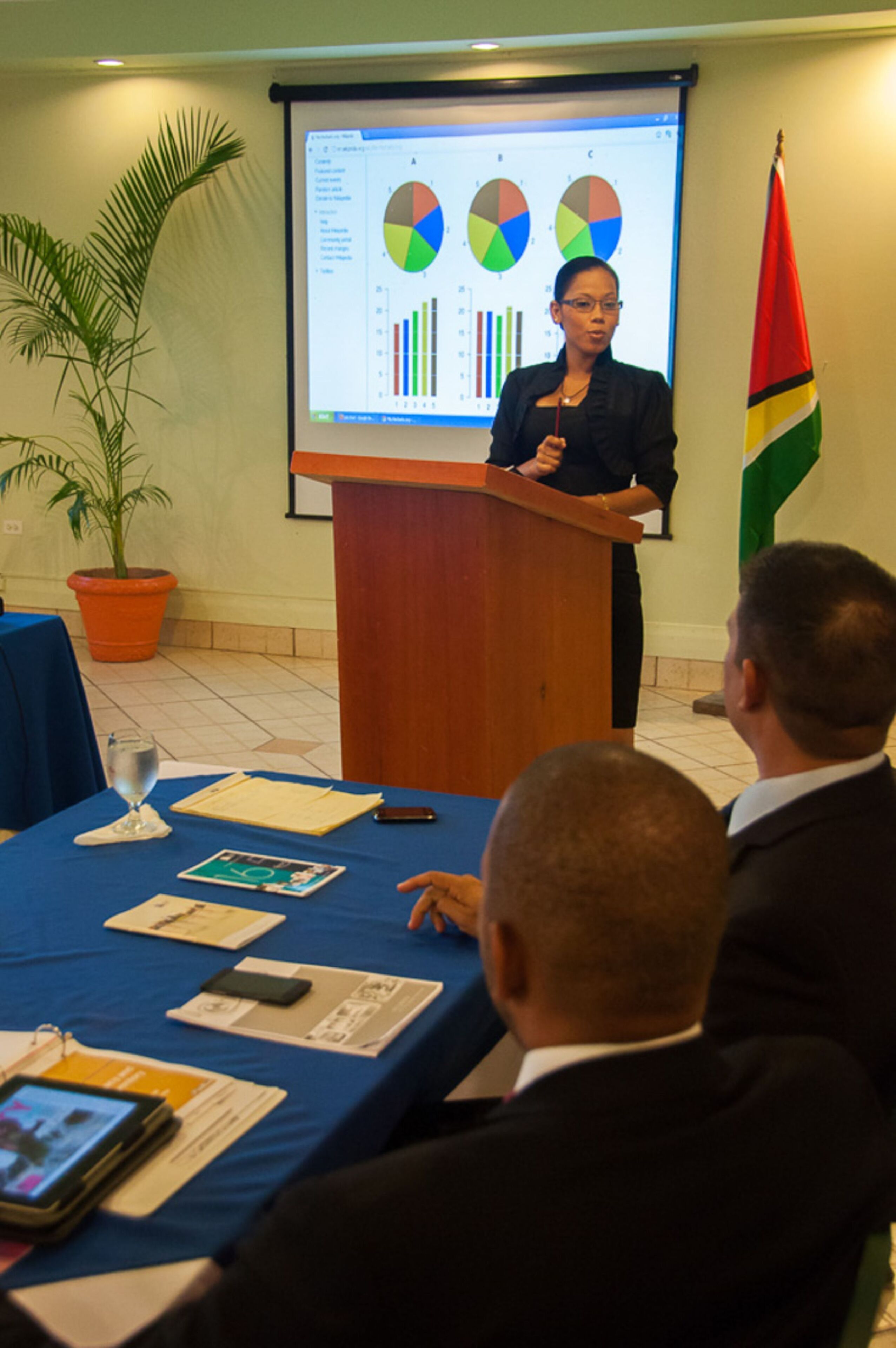 A person presenting at a podium with a screen displaying charts and graphs.