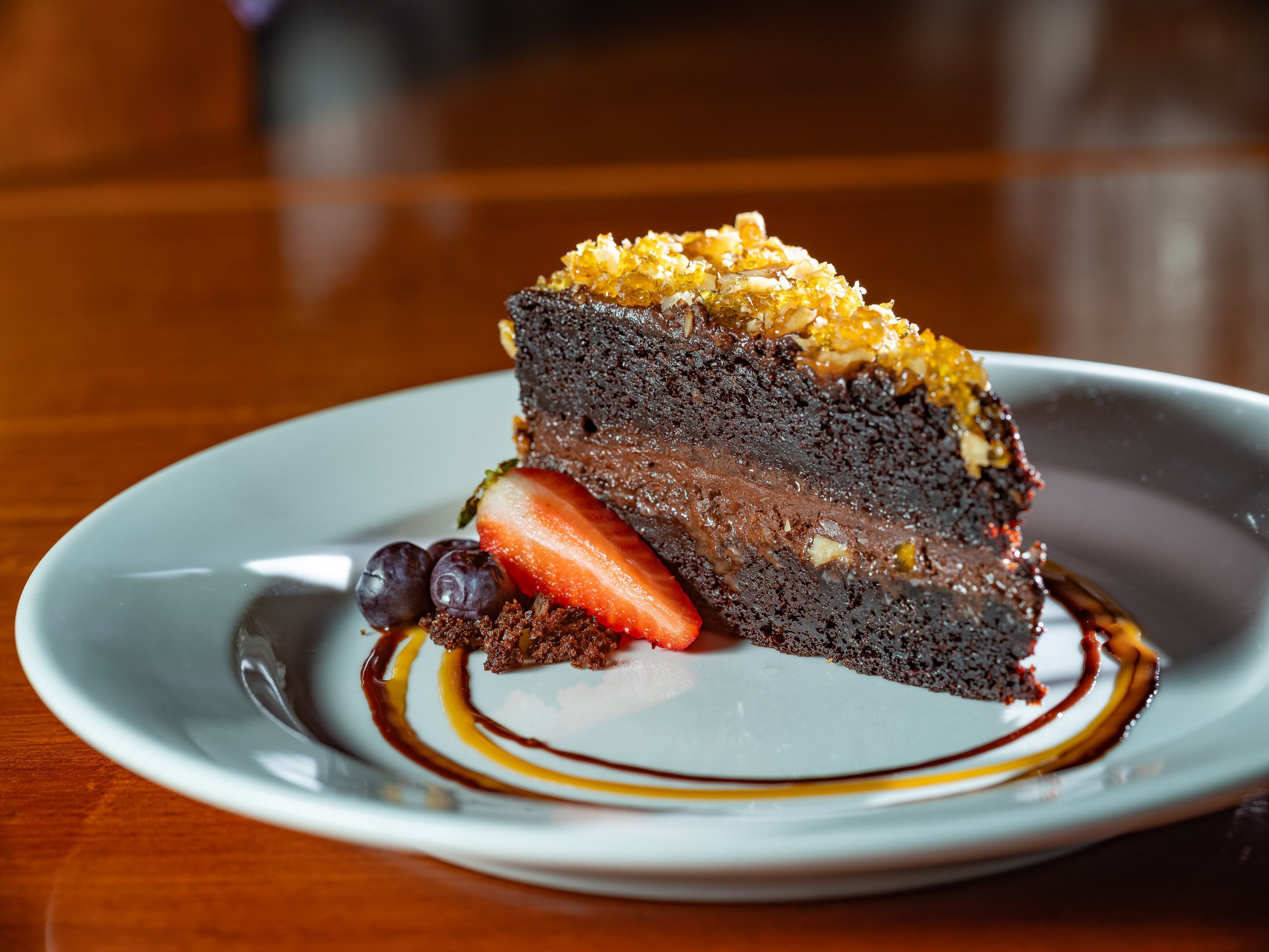Uma fatia de bolo de chocolate com cobertura dourada e calda escorrendo sobre o prato.