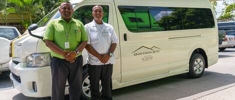 Zwei Männer stehen vor einem weißen Lieferwagen mit der Aufschrift "Grand Coastal Hotel" und Kontaktinformationen.