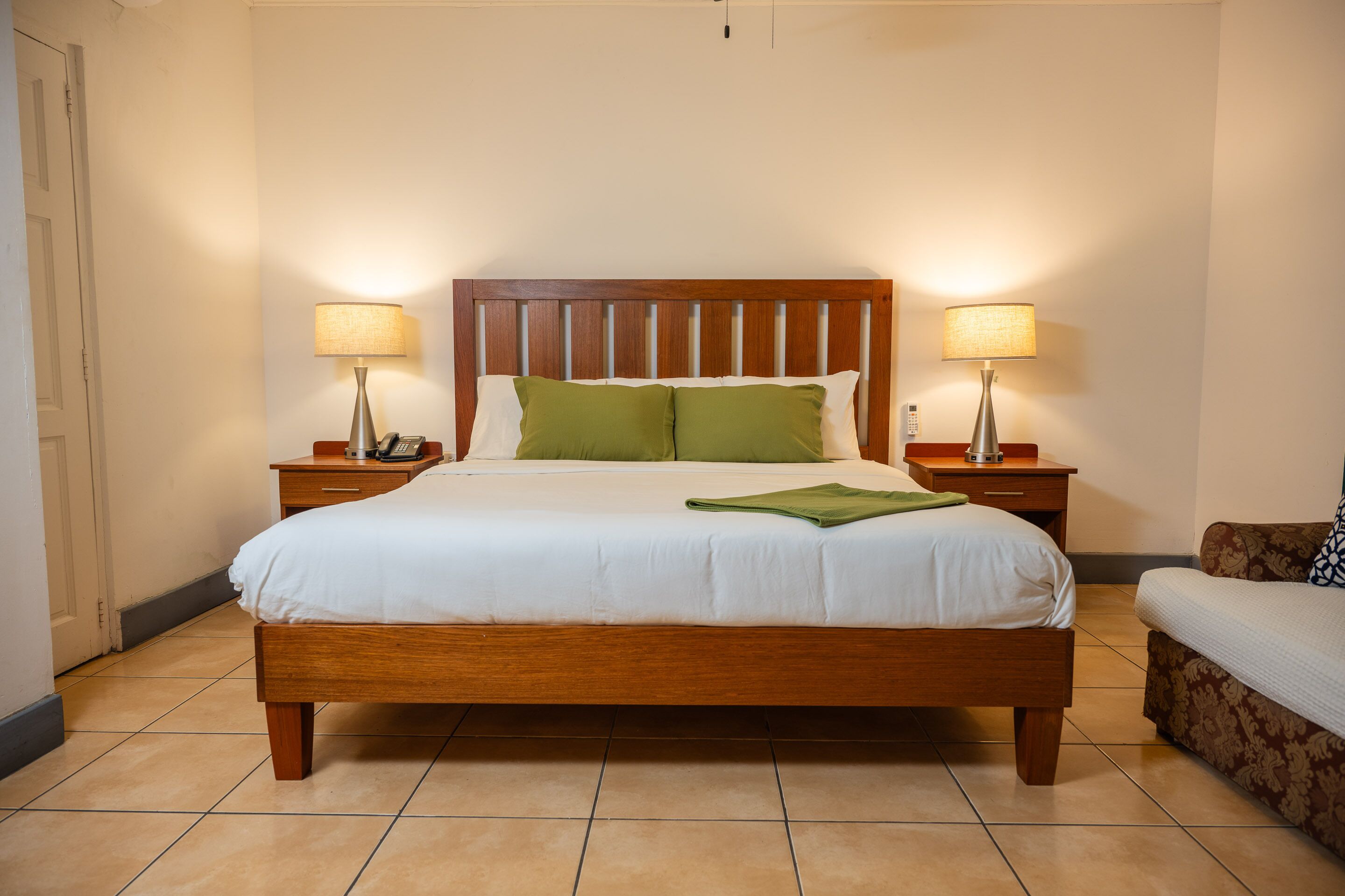 A neatly made bed with a wooden headboard, two bedside tables with lamps, and a small sofa.