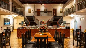 Un vaste espace dédié à la salle à manger, avec une grande table en bois au centre, entourée de chaises, un escalier reliant deux niveaux, et un coin cuisine doté d’un comptoir et de tabourets.
