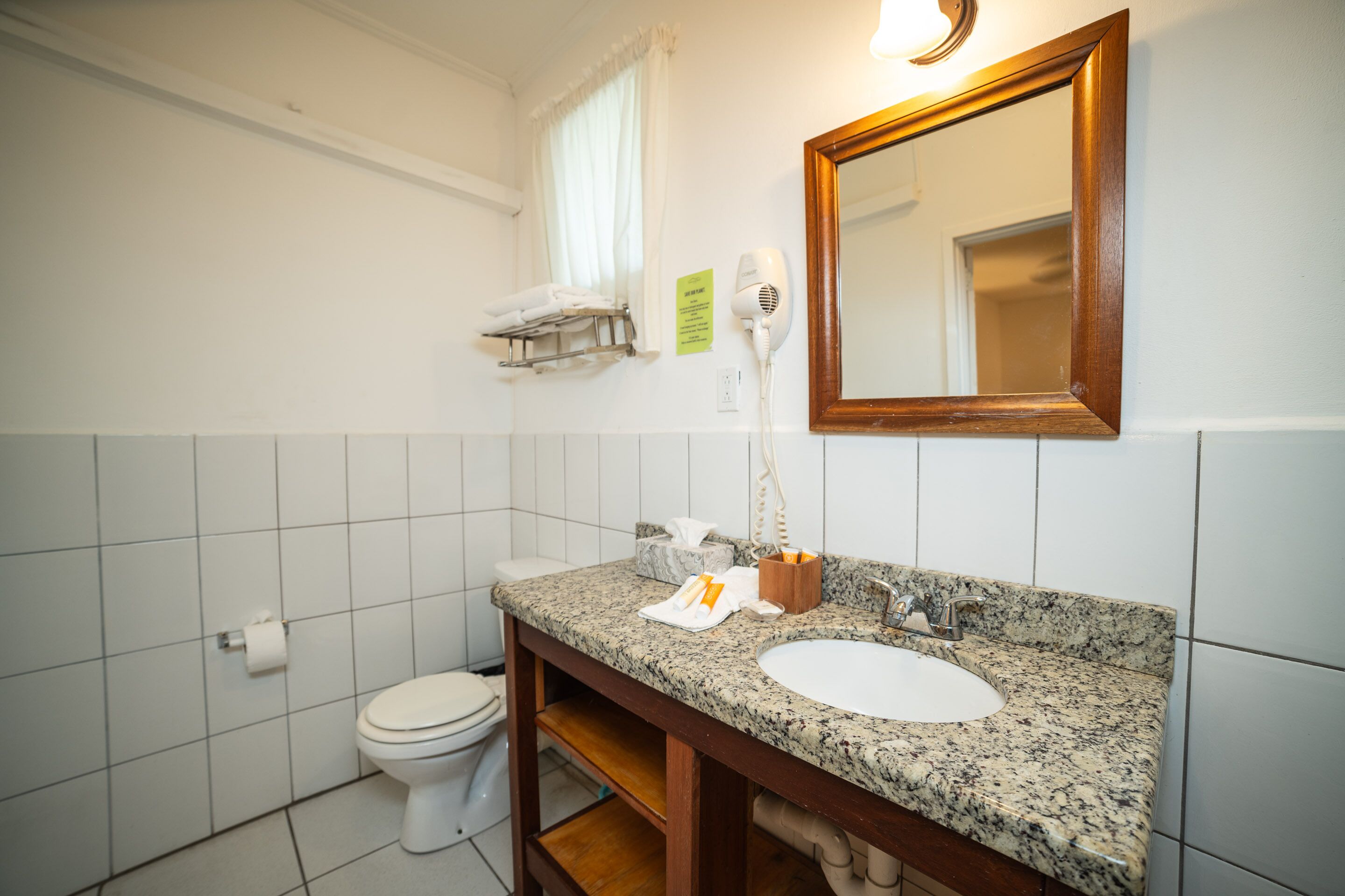 A bathroom with a white toilet, a sink with a marble countertop, a mirror, and a hairdryer on the wall.