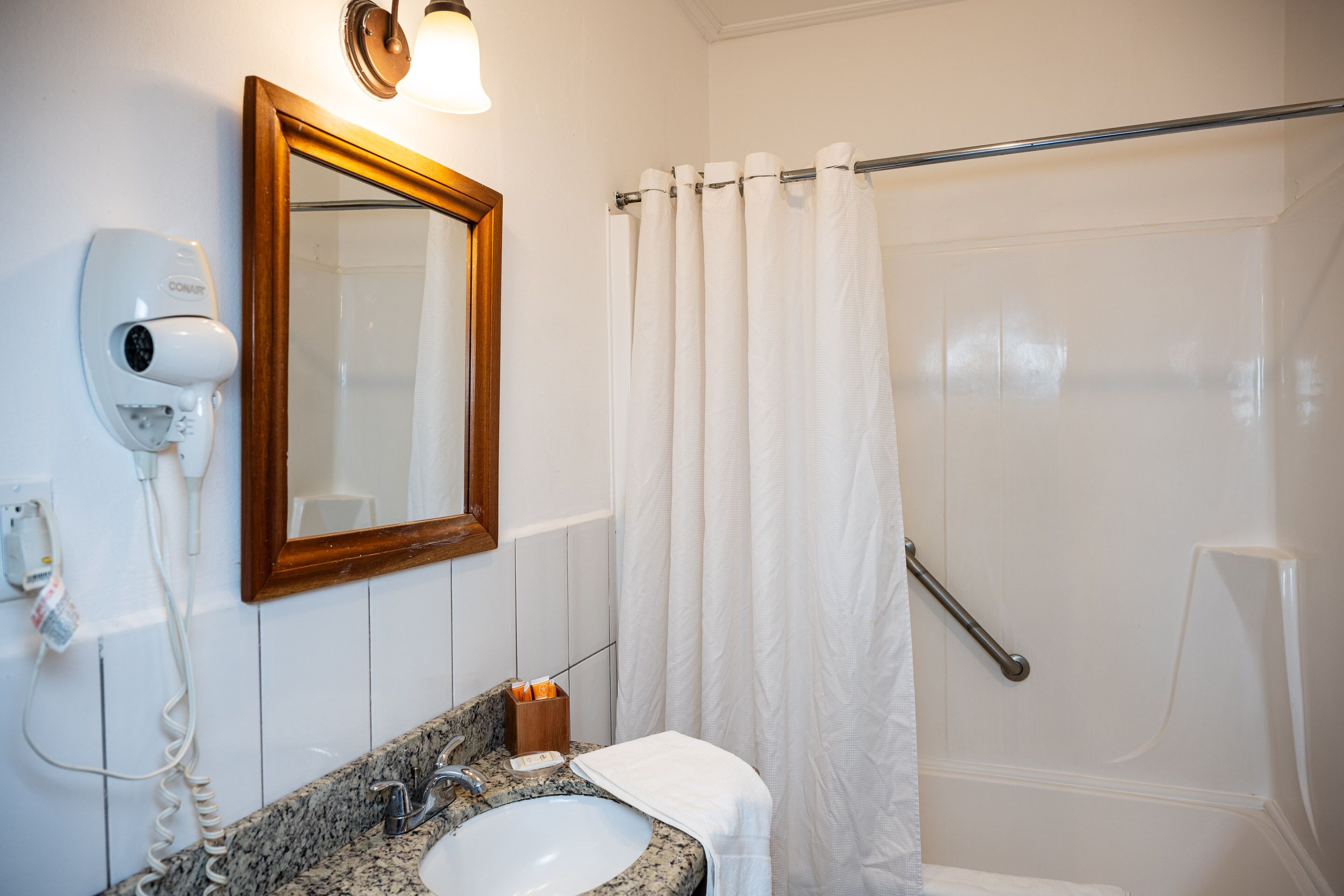 Une salle de bain équipée d’un lavabo, d’un miroir, d’un sèche-cheveux et d’un rideau de douche.