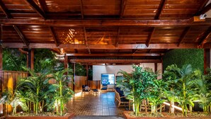 Un espace patio intérieur doté d’un plancher en bois, d’un plafond en bois et d’un mur végétal. On y trouve plusieurs chaises et tables disposées pour créer un espace de détente.