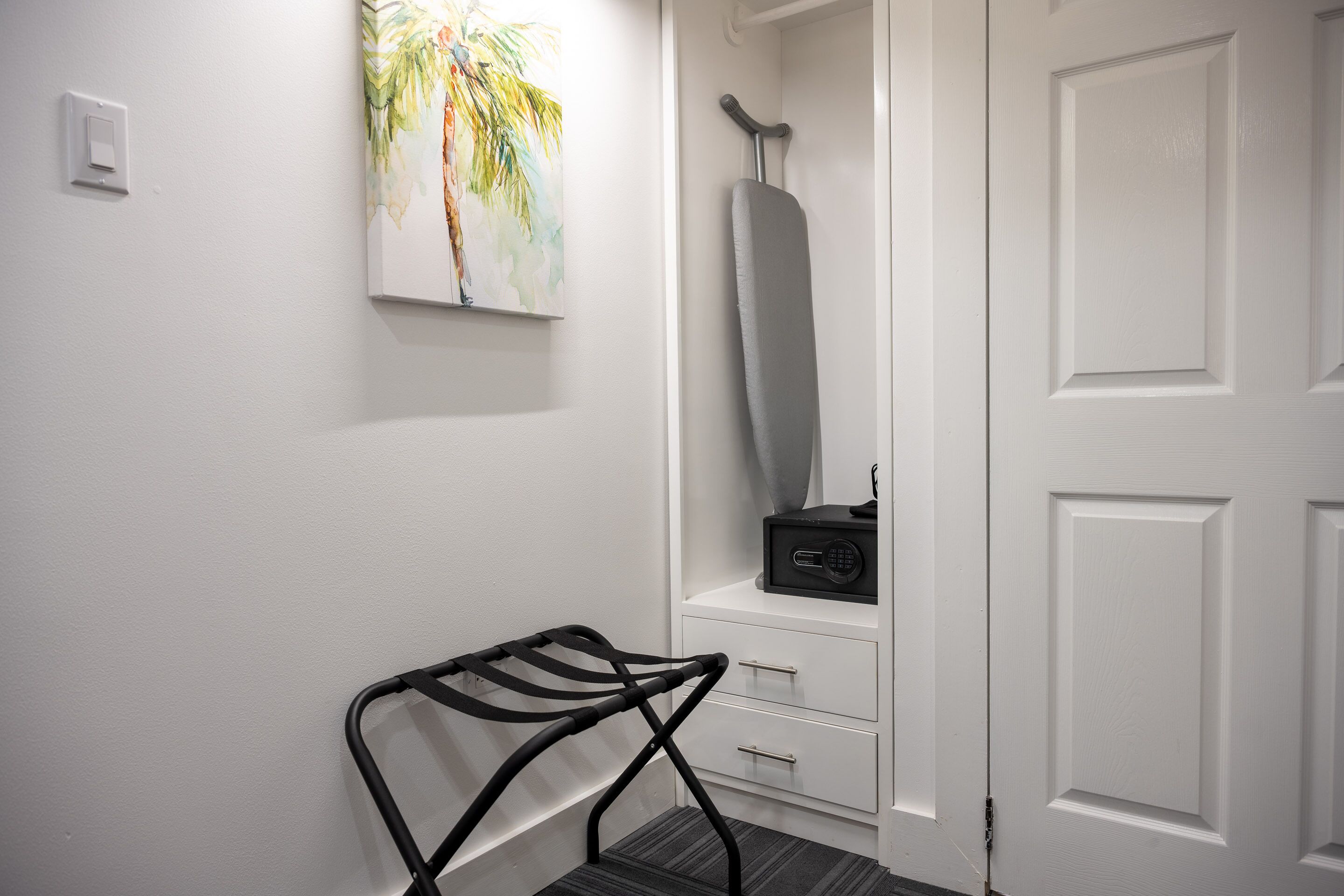 A hallway with a white door, a black chair, a white cabinet, and a painting on the wall.