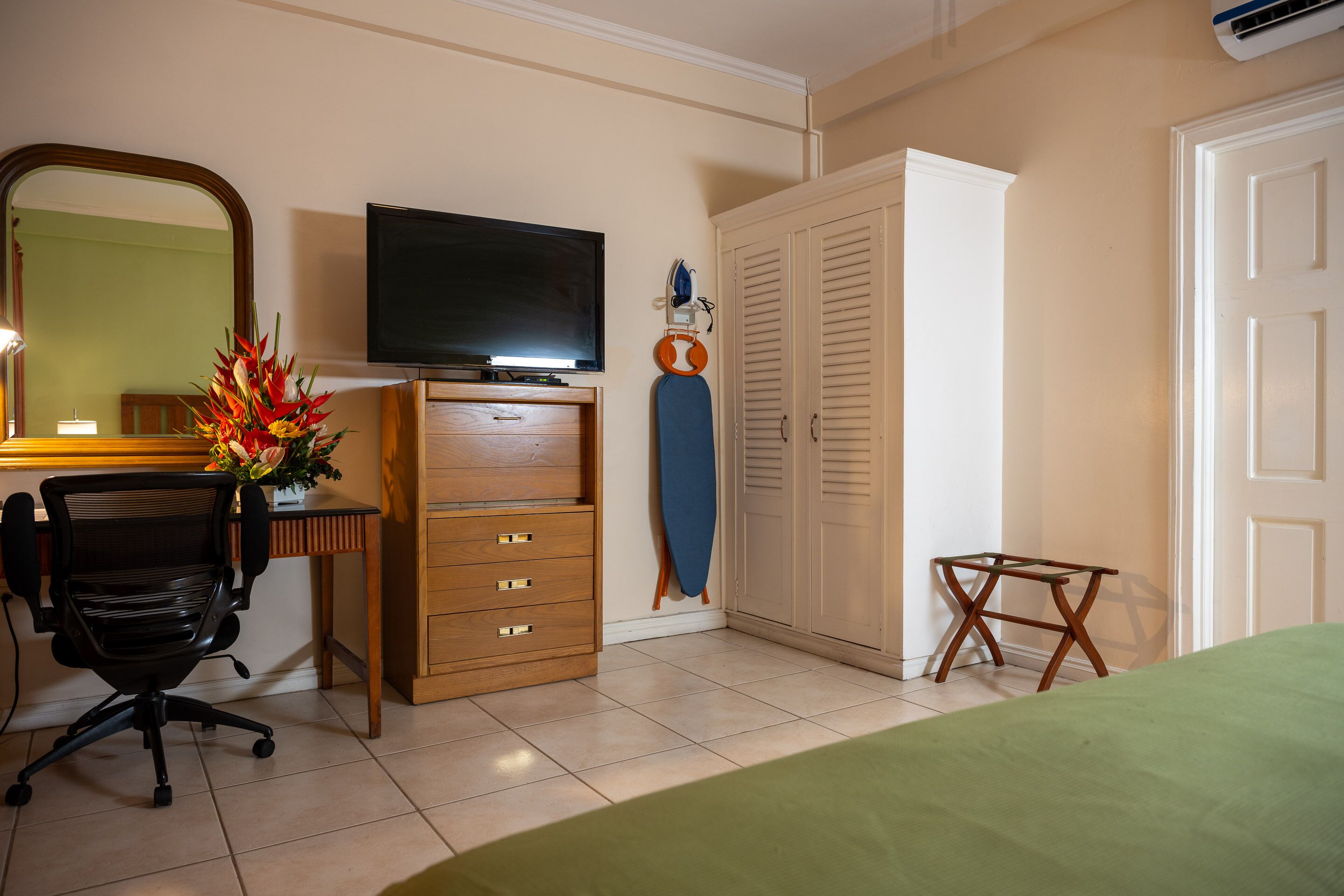 A bedroom with a bed, a desk with a chair, a television, a wardrobe, and a small table.