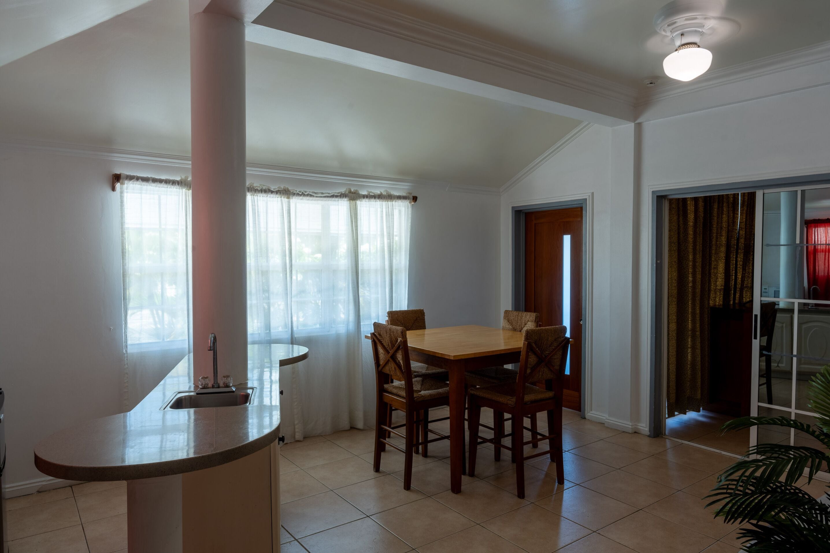 A dining area with a wooden table and chairs, a kitchen counter, and a large window with curtains.