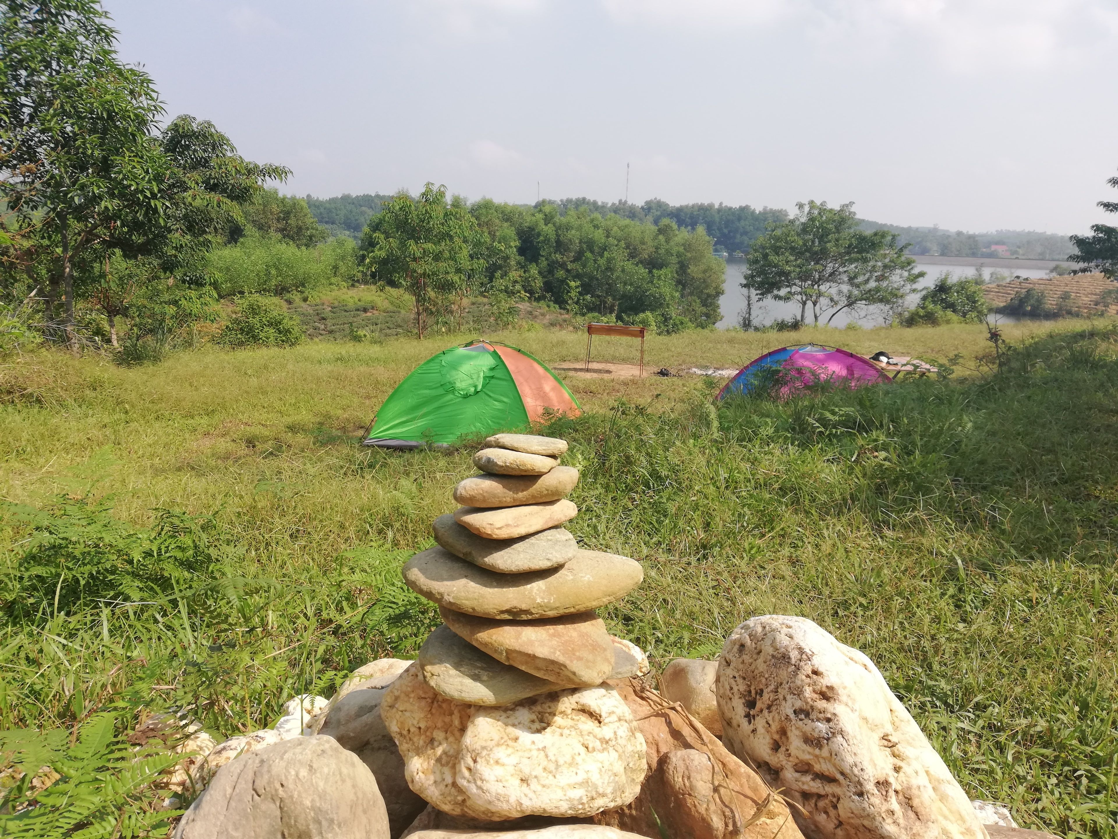 A grassy field with two tents and a stack of stones.